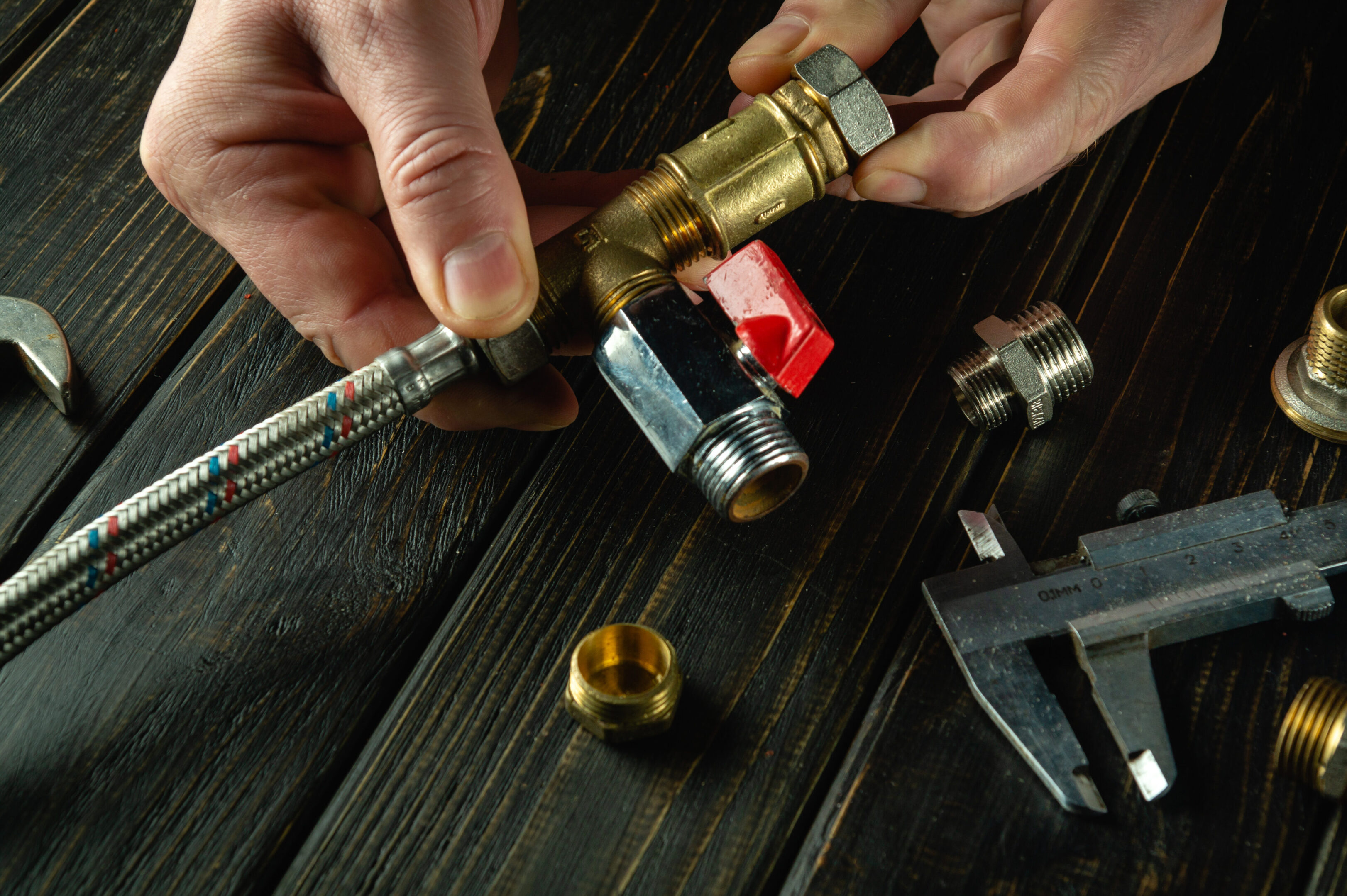 Master plumber connects brass fittings to a plumbing faucet. Installation of gas equipment. Close-up of a master hands while working in a workshop.