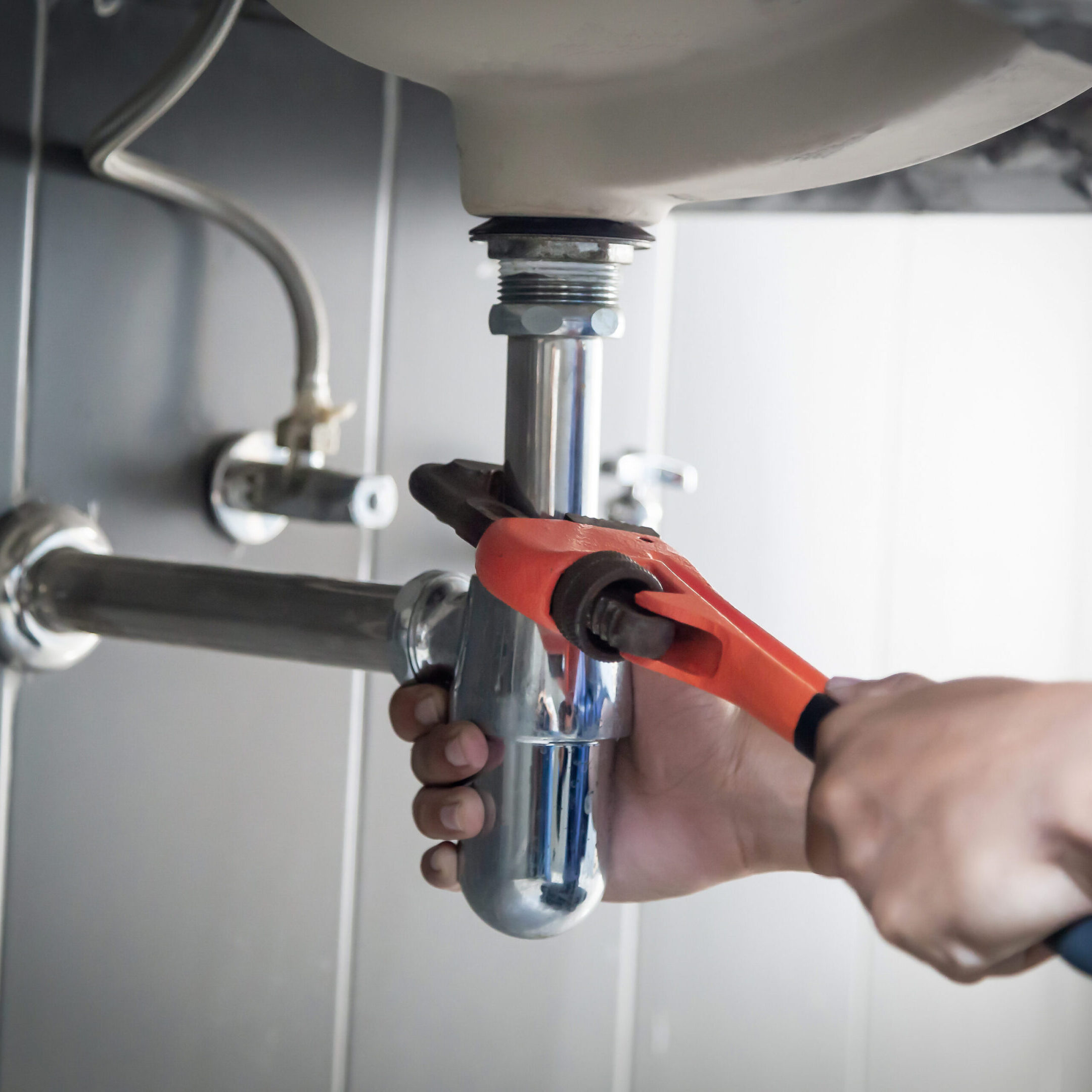 Plumber uses wrench to repair water pipe under sink There is maintenance to fix the water leak in the bathroom.with red wrench, plumbing install concept.