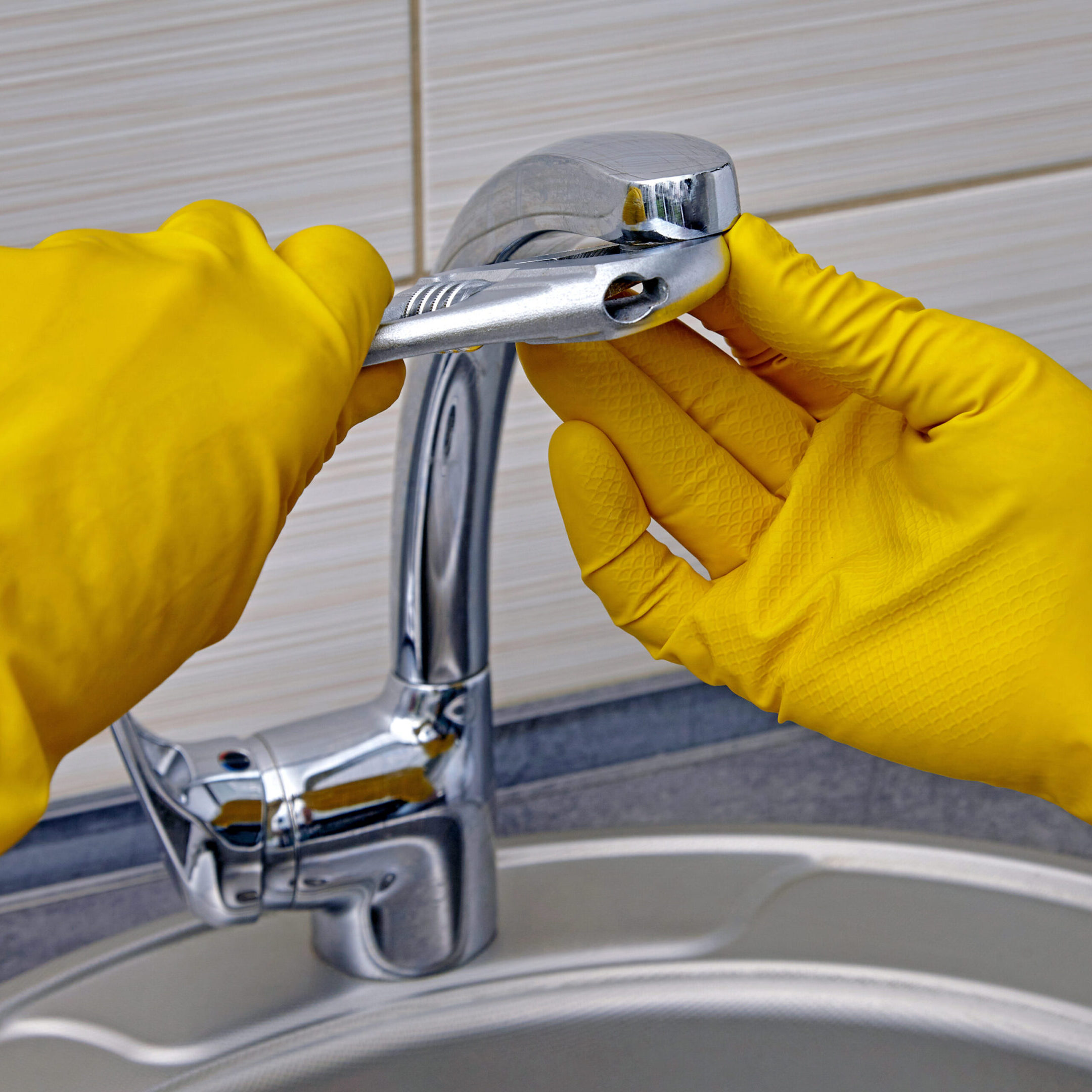 Kitchen faucet repair. A worker in yellow rubber gloves uses an adjustable wrench to unscrew the aerator.