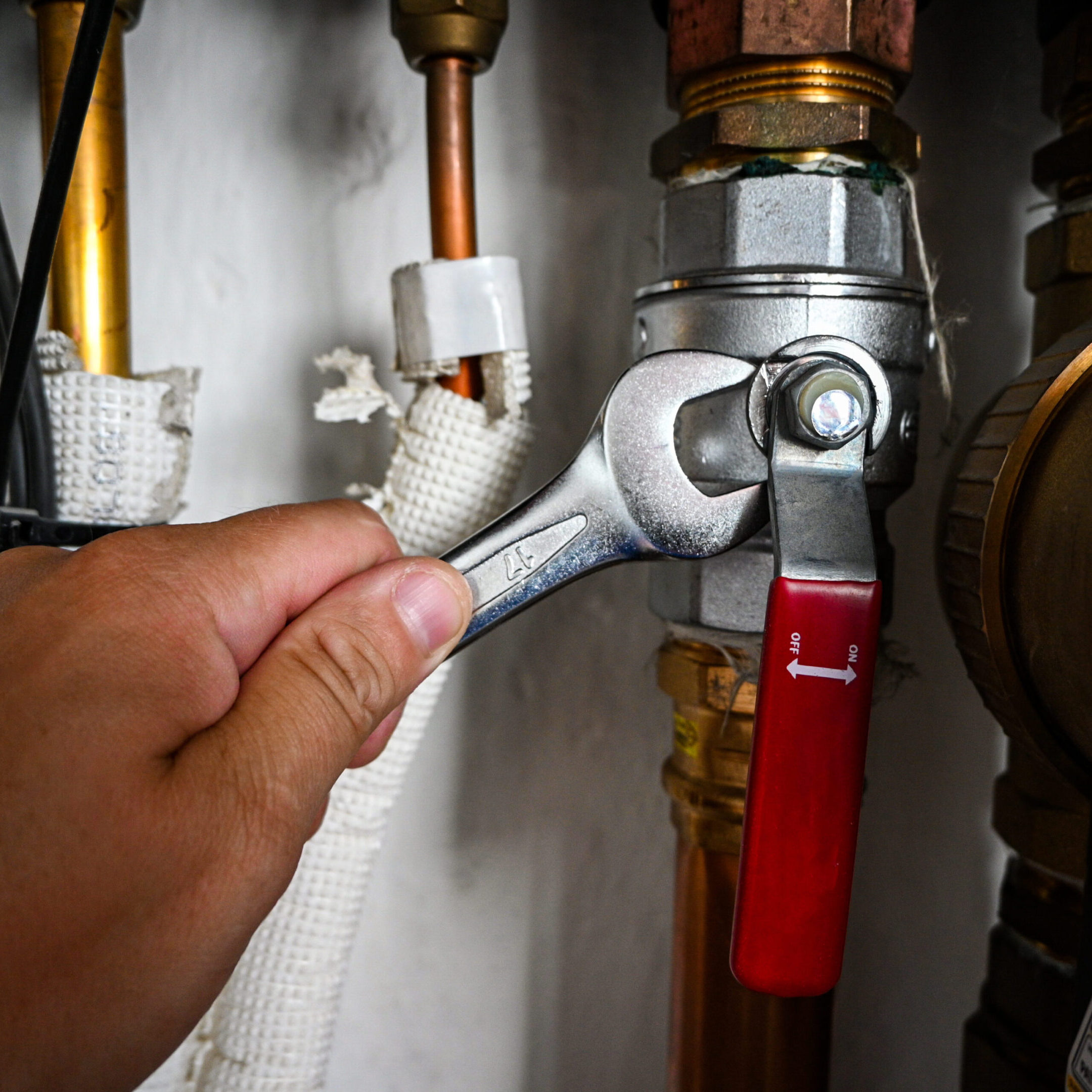 Plumber is tightening a nut on a water heater pipe using an adjustable wrench.